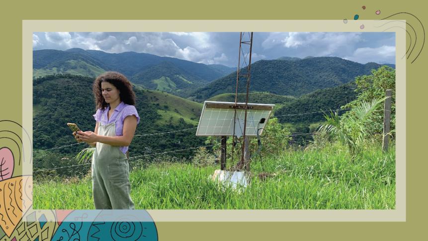 Image of a woman standing on a lush, green mountaintop, testing a newly installed antenna.